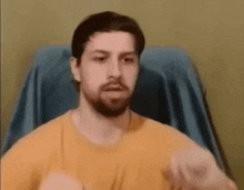a man with a beard is sitting in a chair wearing a yellow shirt and making a funny face .