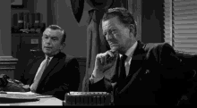 a man in a suit sits at a desk in front of a typewriter