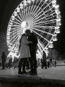a couple kissing in front of a large ferris wheel