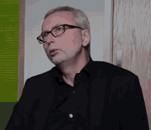 a man wearing glasses and a black shirt looks to his left