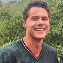 a young man with curly hair is smiling and wearing a green shirt