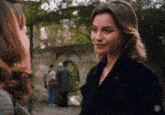 a woman in a black coat talks to another woman in a park