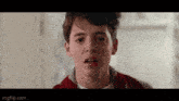 a young man in a red jacket is making a funny face in a room .
