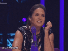 a woman sitting in front of a purple microphone with the username lialmeida05 on the bottom