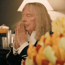 a man with long blonde hair is praying in front of a table full of fruit