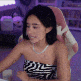 a woman wearing a zebra print top is sitting in a pink and white chair