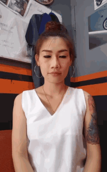 a woman with a tattoo on her arm wearing a white tank top
