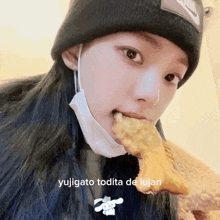 a woman wearing a mask and a beanie is eating a piece of food