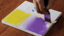 a person is painting a yellow and purple painting on a canvas