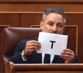 a man in a suit and tie holds up a piece of paper with the letter t on it