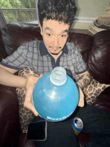 a man is sitting on a couch holding a blue bottle that says buxom