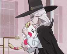 a woman in a black hat holds a stuffed animal with the letter v on its face