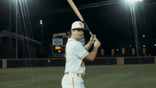 a baseball player is holding a bat in front of a scoreboard that says claude field
