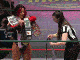 a female wrestler is standing in a ring with a referee and holding a championship belt .