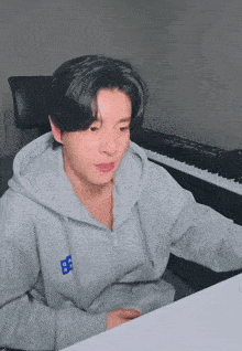 a man wearing a grey hoodie with the letter b on it sits in front of a keyboard