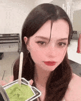 a woman is holding a container of green ice cream with a stick in it