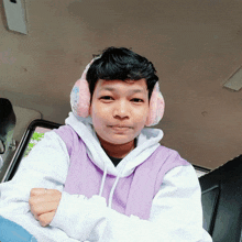 a man wearing ear muffs and a purple hoodie looks at the camera
