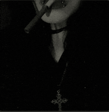 a woman is smoking a cigarette with a cross necklace around her neck