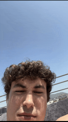 a young man with curly hair takes a selfie with a blue sky in the background