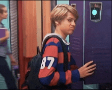 a young boy with a backpack is standing in front of a locker .