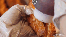 a person is pouring sauce on a croissant with the words made in animotica visible in the corner
