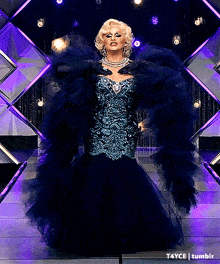 a drag queen wearing a blue dress and gloves is standing on a stage