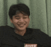 a young man wearing a river sweatshirt is smiling and looking at the camera .