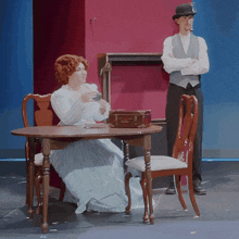 a woman sits at a table while a man stands behind her