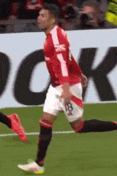 a soccer player wearing a red and white jersey with the number 18 on it is running on the field .