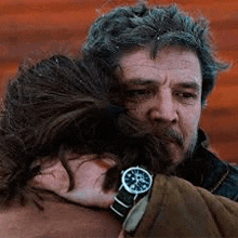 a man with a beard is hugging a woman with a watch on her wrist .
