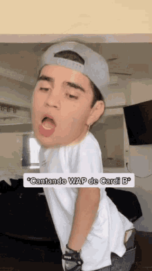 a young man wearing a baseball cap and a white shirt is singing the song cantando wap de cardi b