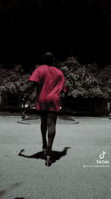 a man wearing a red shirt and shorts is walking down a street at night .