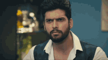 a man with a beard is wearing a white shirt and blue vest