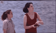 two women are standing next to each other in front of a body of water . one woman is pointing at the water .