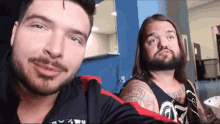 a man with long hair and a beard is wearing a black tank top with a tattoo on his arm