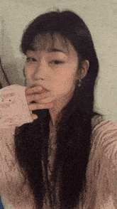 a woman in a pink sweater is taking a selfie with her hand to her mouth