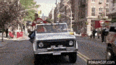 a group of people are riding in a jeep down a street .