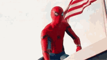 a man in a spiderman costume is holding an american flag while standing on top of a building .