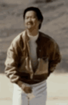 a man wearing a brown jacket and white pants is standing on a beach .