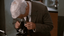 a man in a suit and tie is looking through a microscope in a lab .