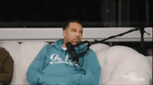 a man in a blue hoodie is sitting on a couch with a microphone .