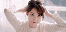 a woman in a white sweater is holding her hair in a bun and smiling .