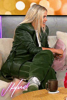a woman in a green leather suit is sitting on a couch with a cup of coffee on the table .