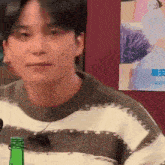 a man in a tie dye sweater is sitting at a table with a green bottle .