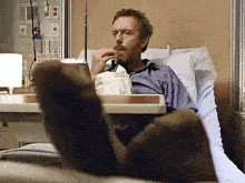 a man laying in a hospital bed with his feet up reading a newspaper