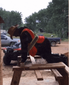 a man in a cowboy hat is kneeling down on a wooden picnic table