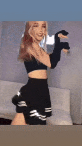 a woman in a black crop top and skirt is dancing in front of a white couch .