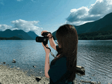 a woman is taking a picture of a lake with a canon camera
