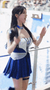 a cheerleader in a blue and white dress is standing on a balcony holding a fan .
