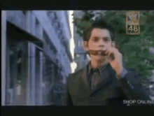 a man in a suit and tie is smoking a cigarette in front of a sign that says 48